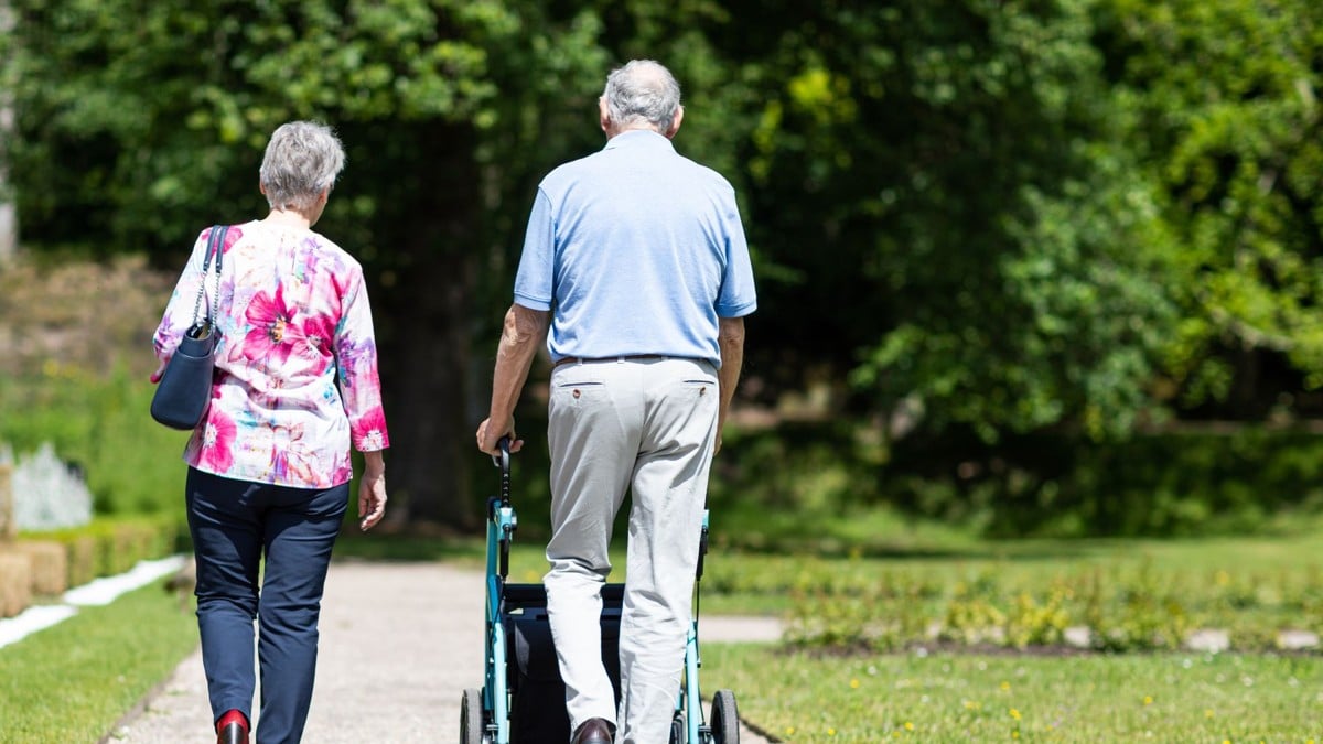 Due persone anziane camminano in un parco, una con un deambulatore.