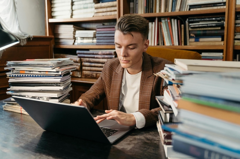 Uomo che studia al computer circondato da libri: conoscenza e pensiero critico nell'era dell'intelligenza artificiale