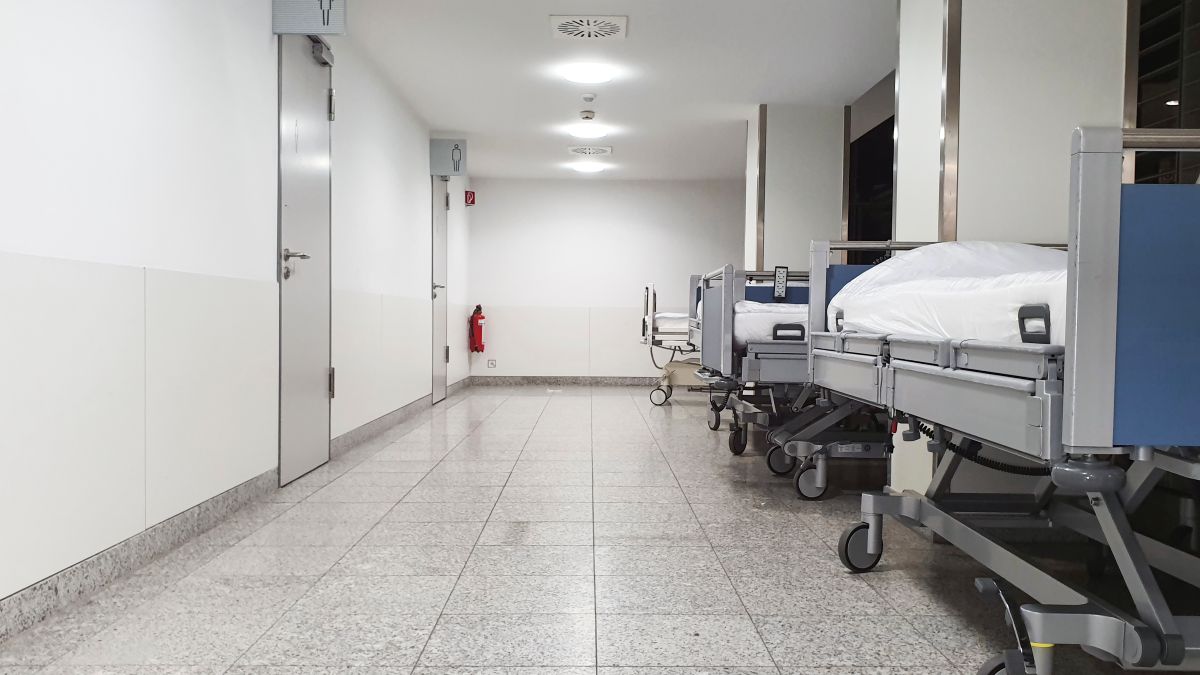 Corridoio ospedaliero con letti vuoti allineati lungo una parete.