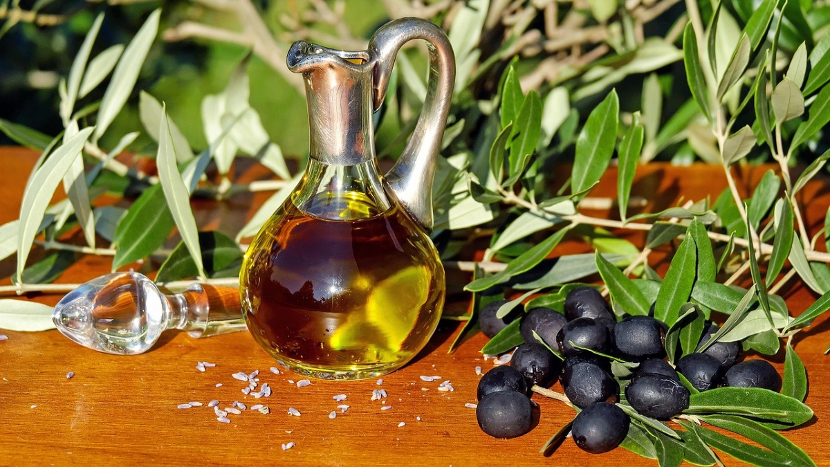 Caraffa di vetro e metallo con olio extravergine di oliva, olive nere e rami di ulivo su un tavolo
