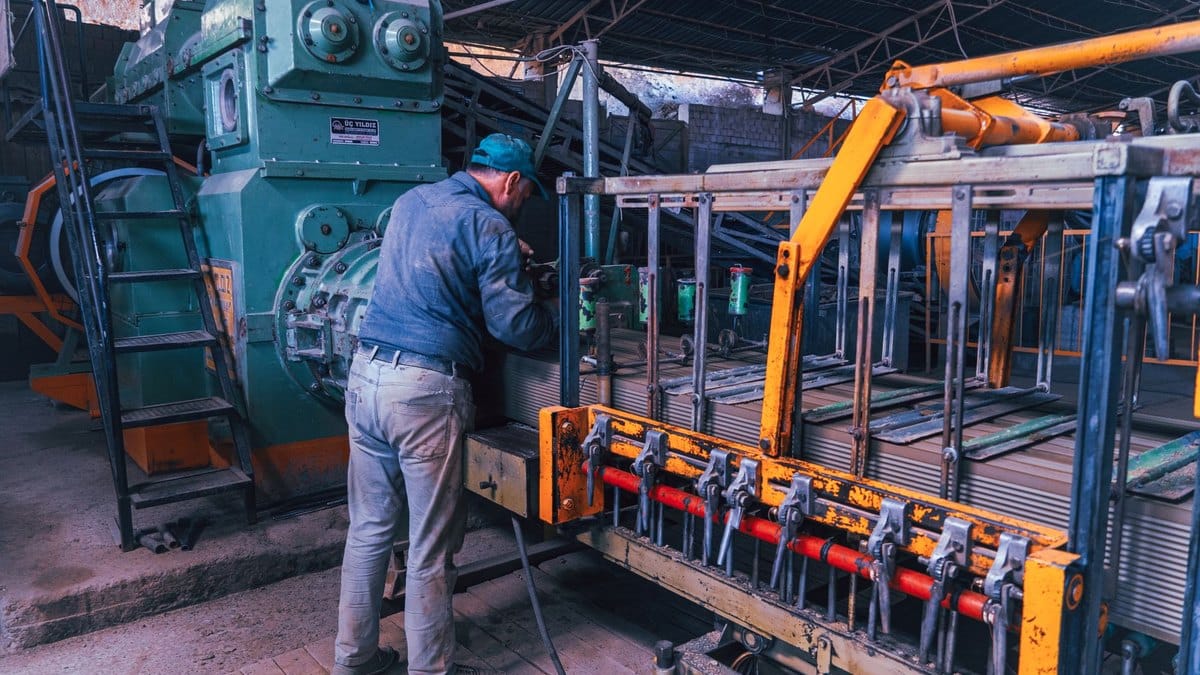 Un lavoratore di spalle interviene su un macchinario in un capannone industriale