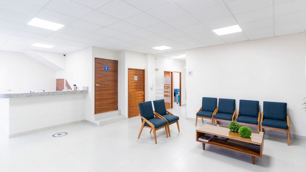 Sala di attesa luminosa con sedute e porte di accesso agli ambulatori.