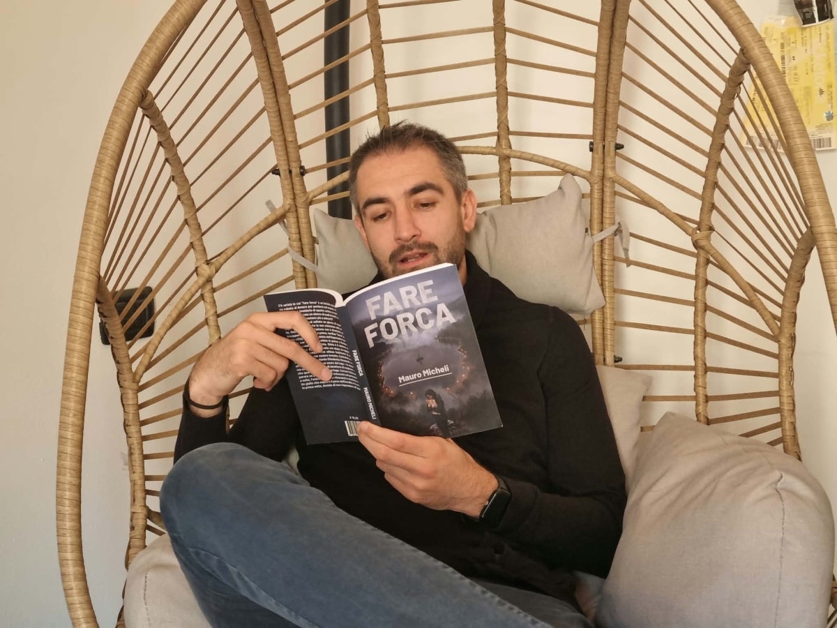 Mauro Micheli legge il romanzo Fare Forca seduto su una poltrona in vimini