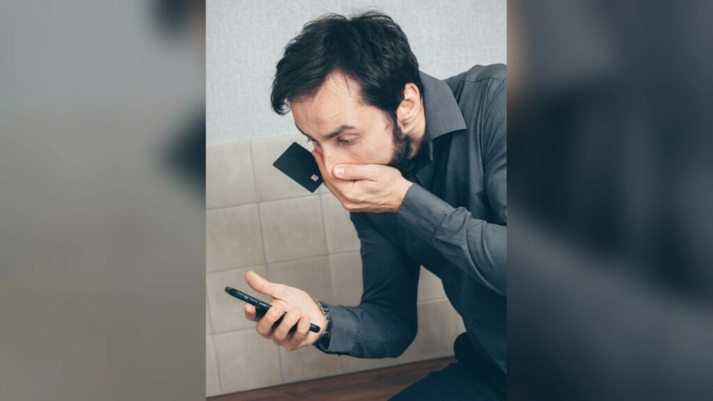 Uomo preoccupato guarda lo smartphone mentre tiene una carta di credito