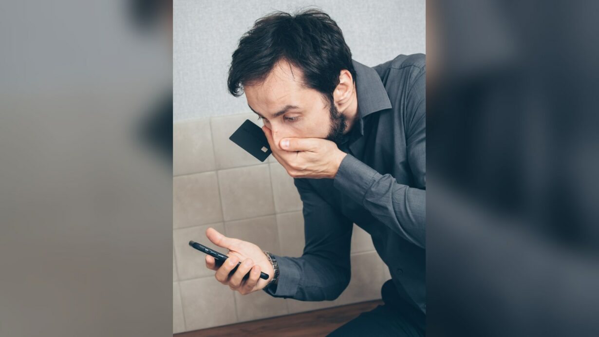 Uomo preoccupato guarda lo smartphone mentre tiene una carta di credito